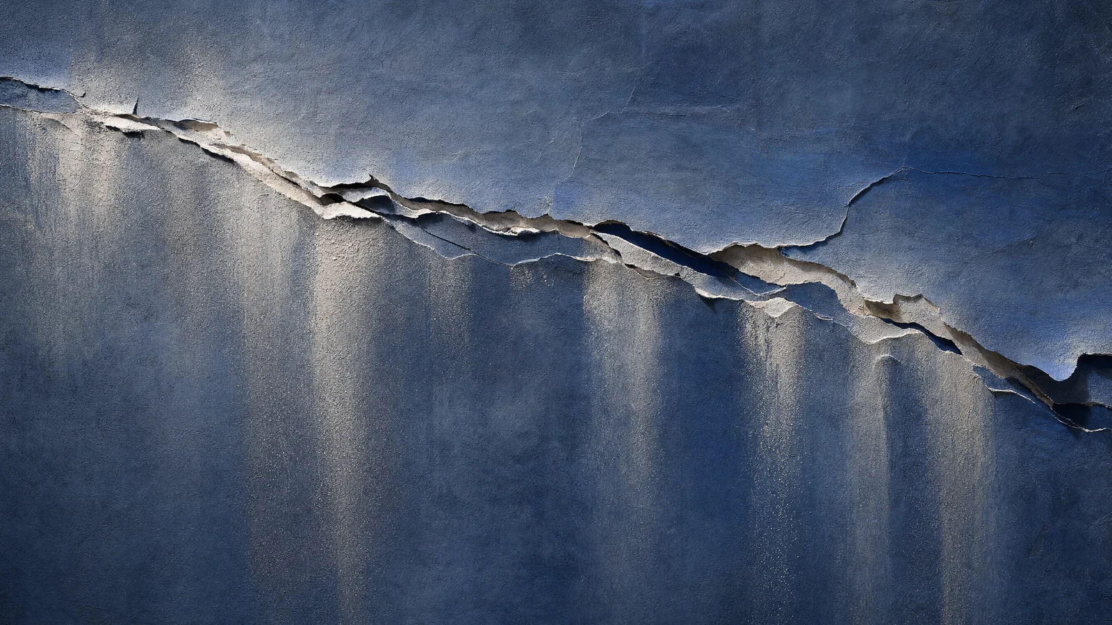 Cracks spreading across a wall, dust drifting down through the light